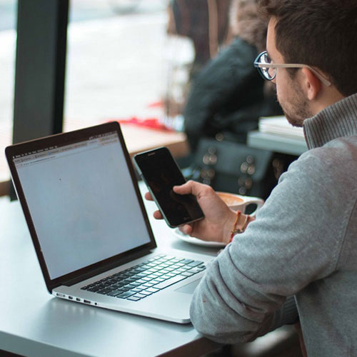 A person using his mobile phone and a laptop